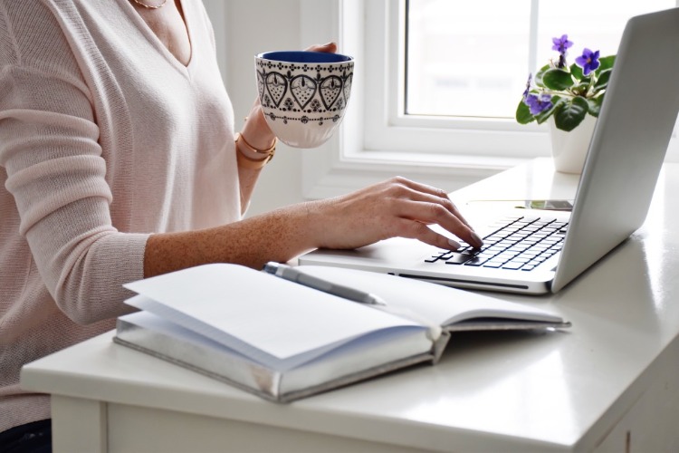 žena so šálkou kávy sedí pred prenosným počítačom pri surfovaní