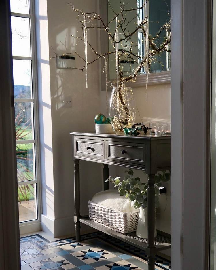 Predsieň na Vianoce zdobí vetvu v sklenenej váze s rozprávkovými svetlami