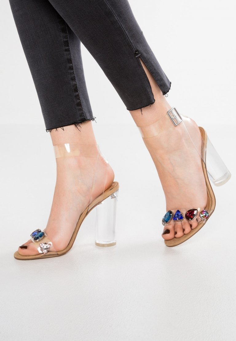 Transparentné sandále na podpätku kombinujú úzke džínsy v čiernej farbe