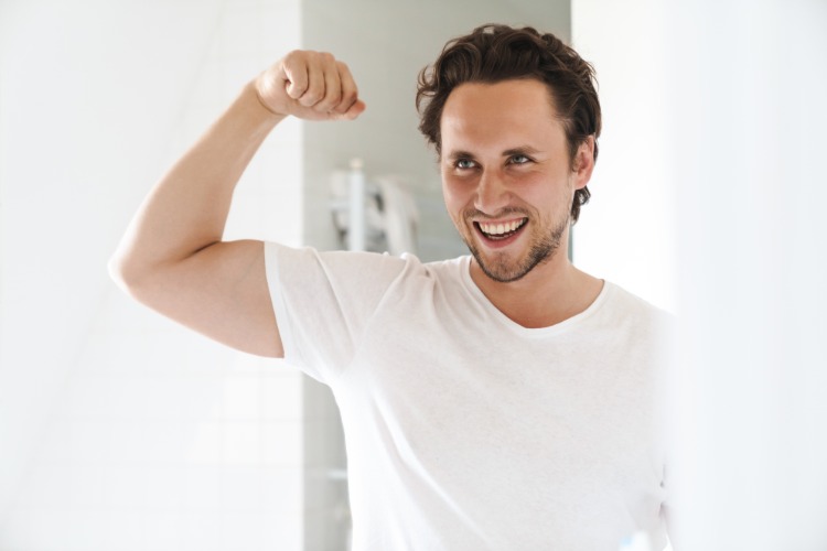 usmievajúci sa muž ukazuje v zrkadle svoje silné svaly