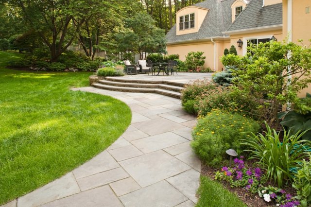 Okraje trávnika z kamenných dosiek tvoria záhonový dom