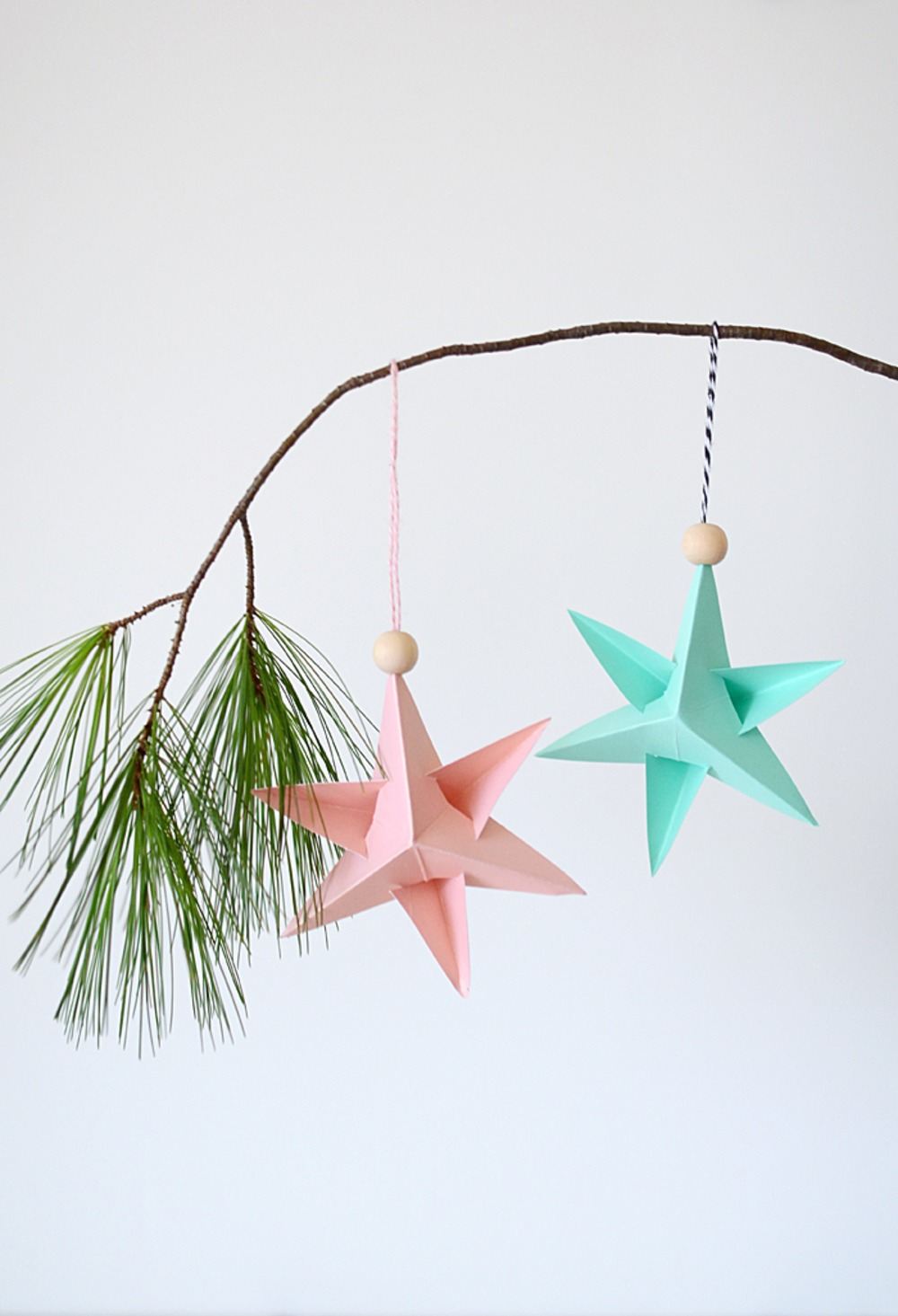 dve hviezdičky z papiera a nití s ​​drevenými korálkami visia na borovicovej vetve