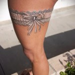 Fénykép egy fehér harisnyakötő tetoválásról a combon