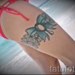 Fotó egy harisnyakötő tetoválásról, kék masnival a fürdőruhás lány combján