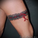 Fotó egy harisnyakötő tetoválásról, piros szalaggal és csipkével