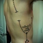 lánc kereszttel és felirattal egy tetováláson egy férfi oldalán