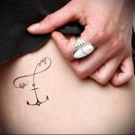 mała kotwica i napis - kobiecy tatuaż z boku