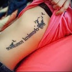 napis w szwach i ptaszki - kobiecy tatuaż na boku