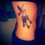 gołąb z kluczami w dziobie - tatuaż z boku kobiety