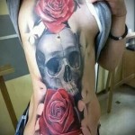 czaszka i dwie czerwone róże - tatuaż z boku kobiety