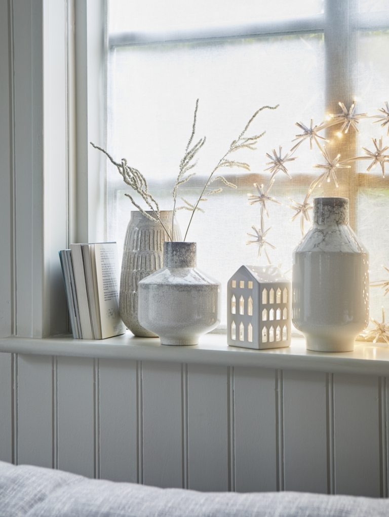Trend farby Vianoce 2019 kompletne v bielej okennej dekorácii s porcelánovými vázami a snehovými vločkami z rozprávkových svetiel