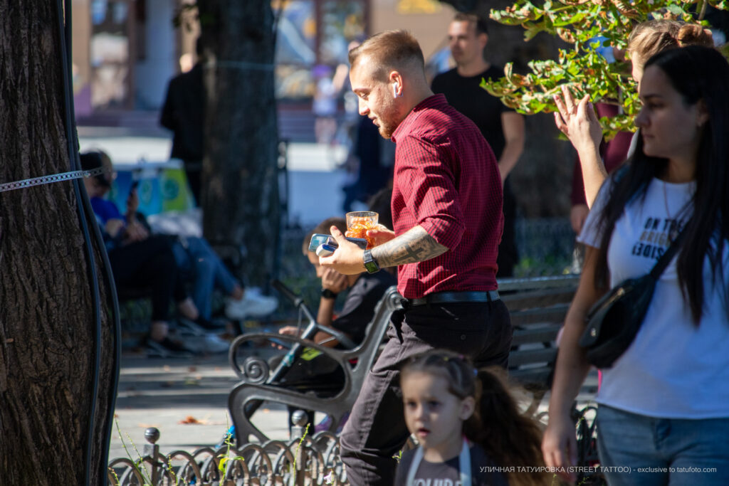 Tatuaż z czarnym krzyżem i geometrycznymi wzorami na lewym ramieniu faceta