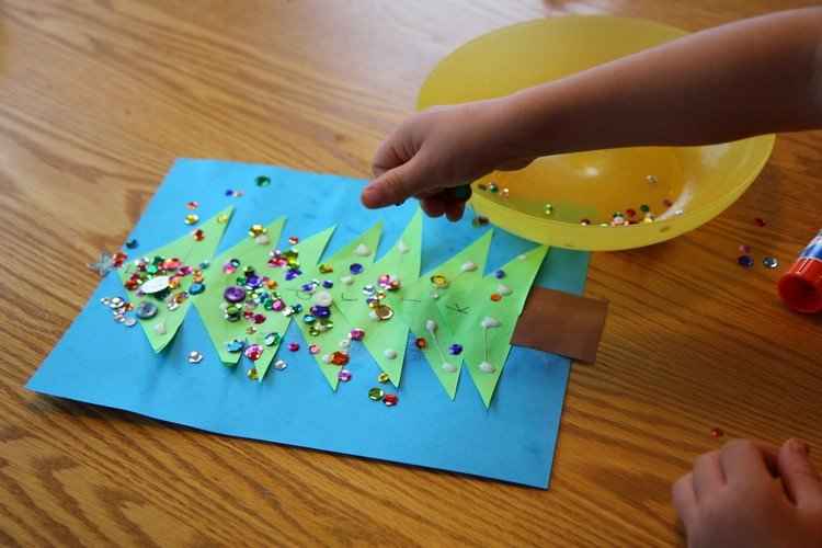 Vianočné remeslá s batoľatami zdobiacimi vianočný stromček z papiera