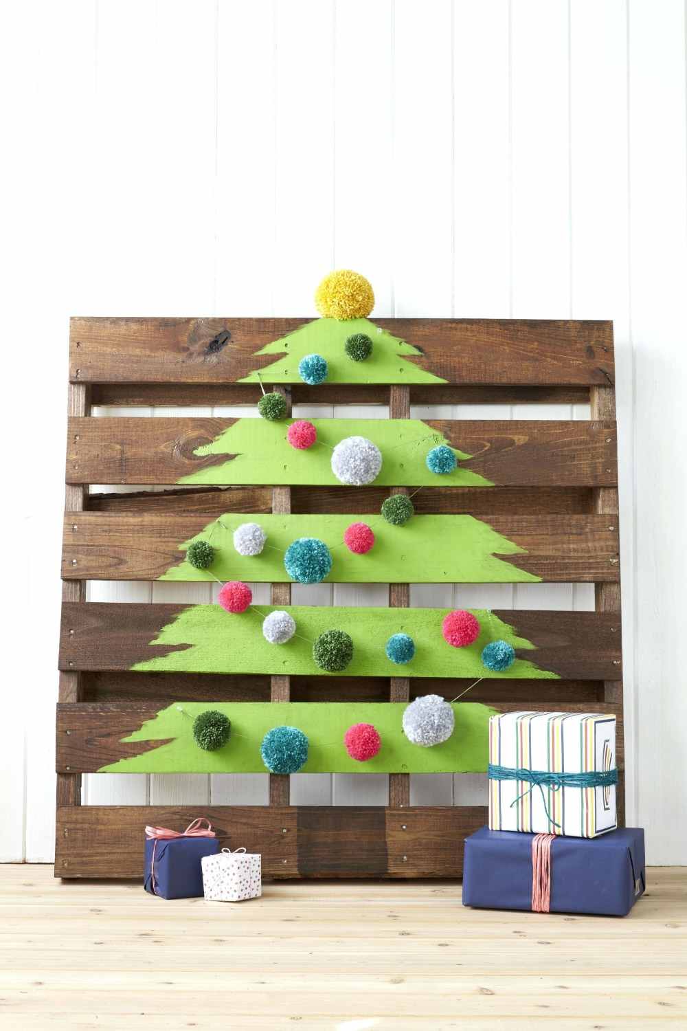 drevená paleta natretá zelenou farbou ako jedľa s cievkami a zabalenými darčekmi