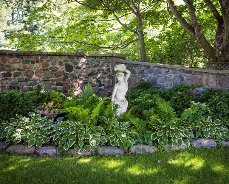 Pekná posteľ so zelenými rastlinami a obkladovými kameňmi na trávniku