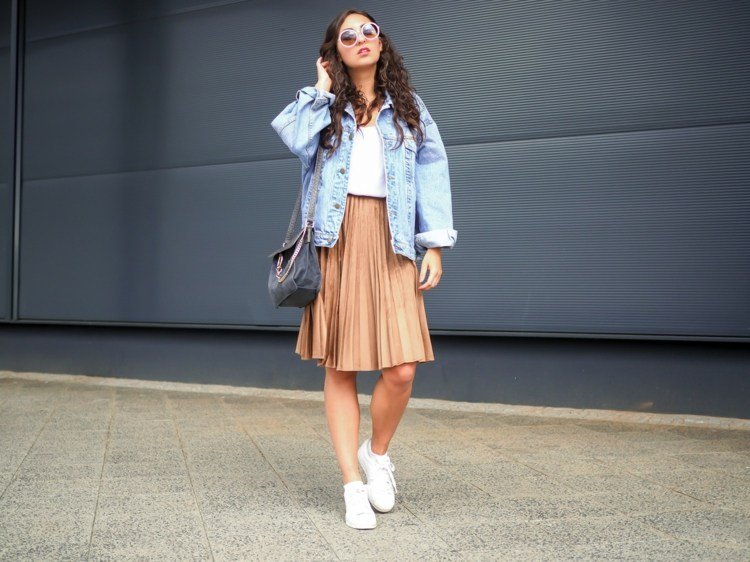 Skladaná sukňa kombinuje letné tenisky denimovú bundu s nadrozmernou koženou kabelkou hnedých vlasov
