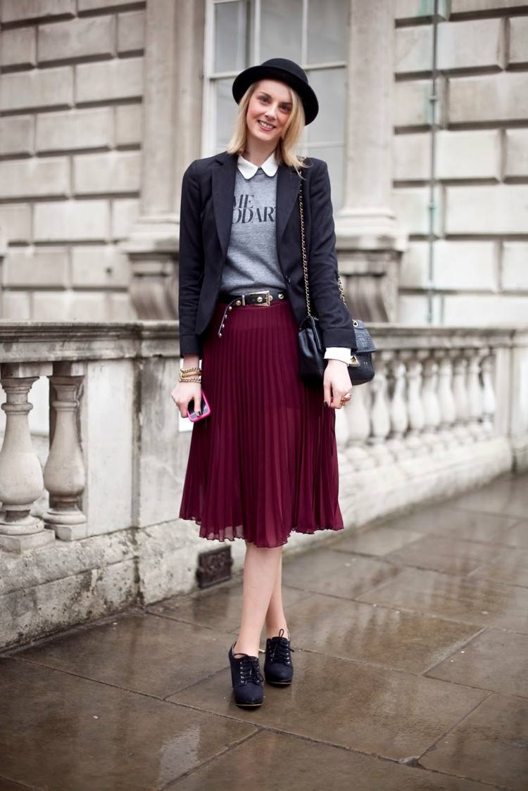 Skladaná sukňa kombinuje bledo šedú mikinu s košeľovou dámskou čiapkou a koženou taškou s krátkymi blond vlasmi