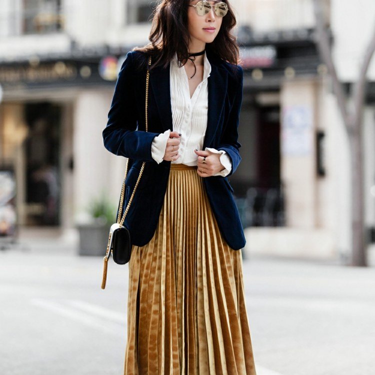 Skladaná sukňa kombinuje zamatovú blejzerovú košeľu a malú kabelku módne trendy 2019