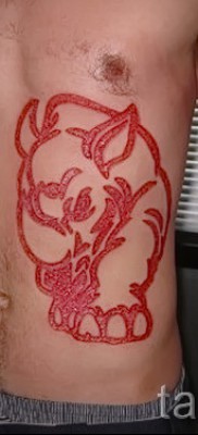 Fotó példa egy orrszarvú tetoválásra - piros tetoválás - egy srác gyomrára és oldalára