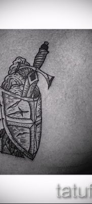 A pajzs és a kard menő tetoválásának fotója közzétételre a karddal ellátott pajzs tetoválásának értelmezéséről